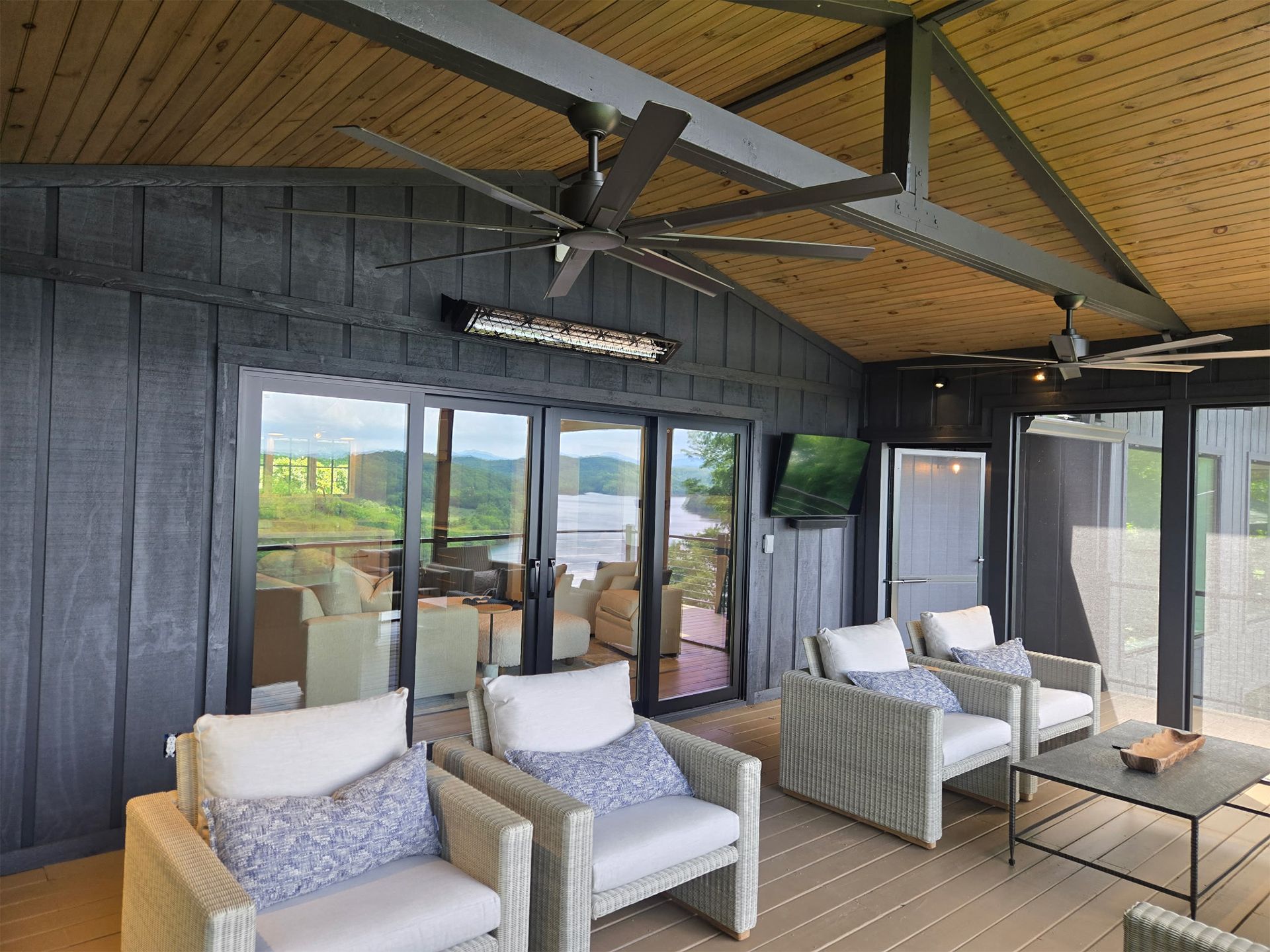 Covered outdoor patio with wicker seating, glass doors, ceiling fans, and a wooden table.