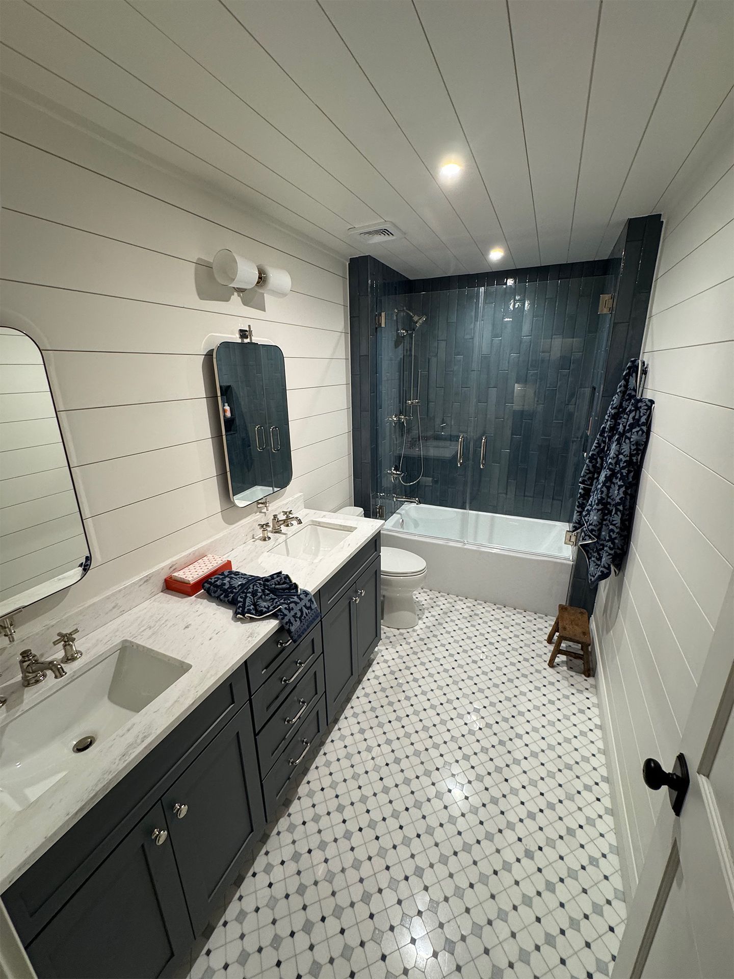Modern bathroom with dark vanity, white shiplap walls, tiled floor, and glass shower enclosure