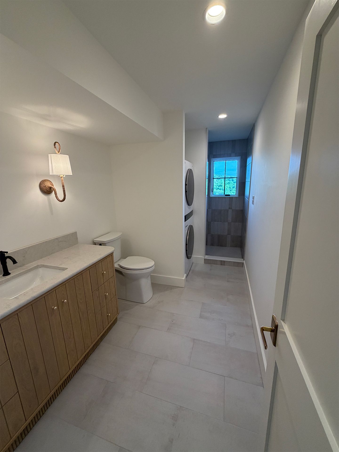 Narrow bathroom with long vanity, toilet, tiled floor, and bright window at the end.