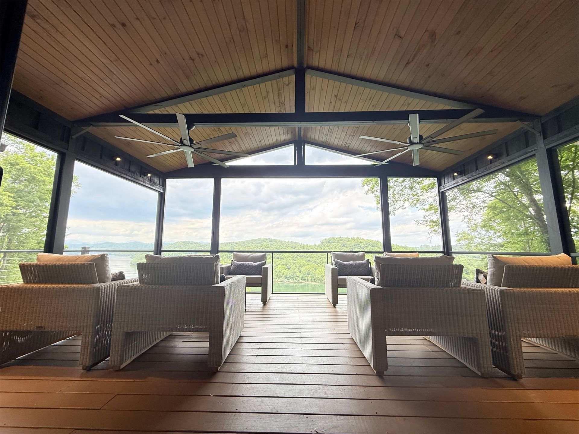 Covered wooden patio with wicker chairs and tables overlooking a lush green landscape