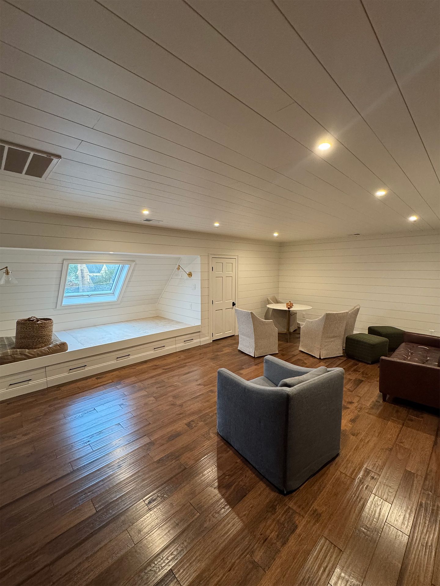 Empty modern living room with wood floors, white walls, and gray chairs facing a wall-mounted TV.