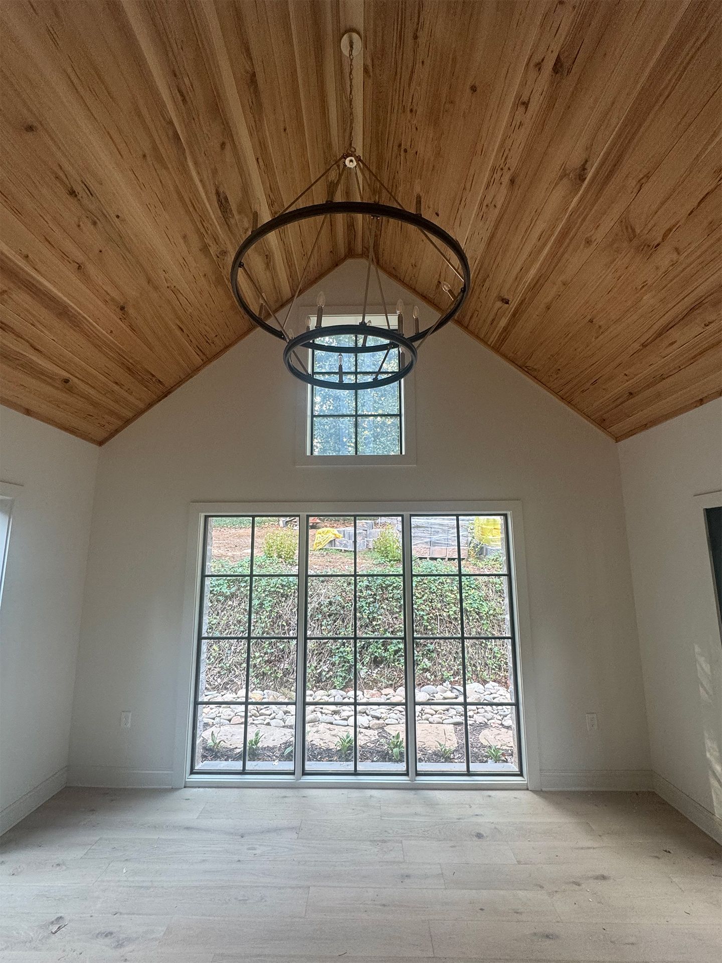 Empty room with wood vaulted ceiling, large front window, and hanging chandelier fixture