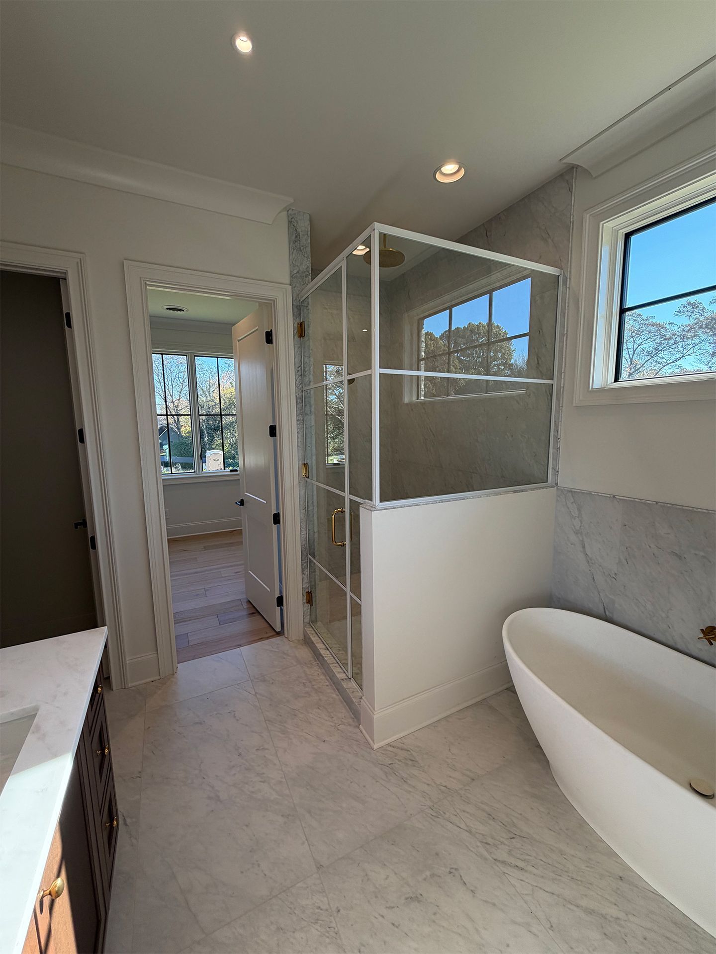 Bright modern bathroom with glass shower, freestanding tub, and large window view
