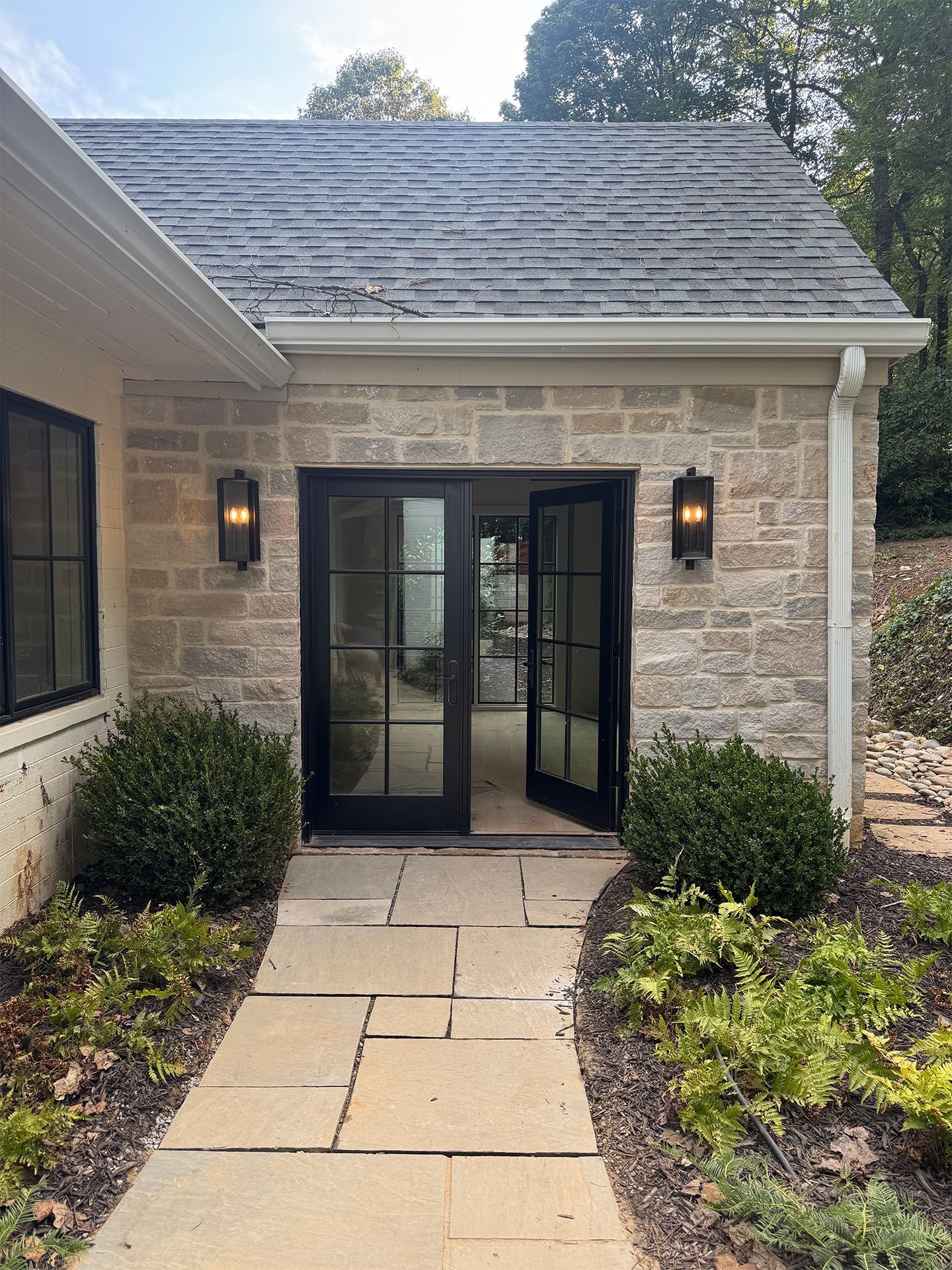 Stone entryway with glass double doors, wall lanterns, and a paved path.