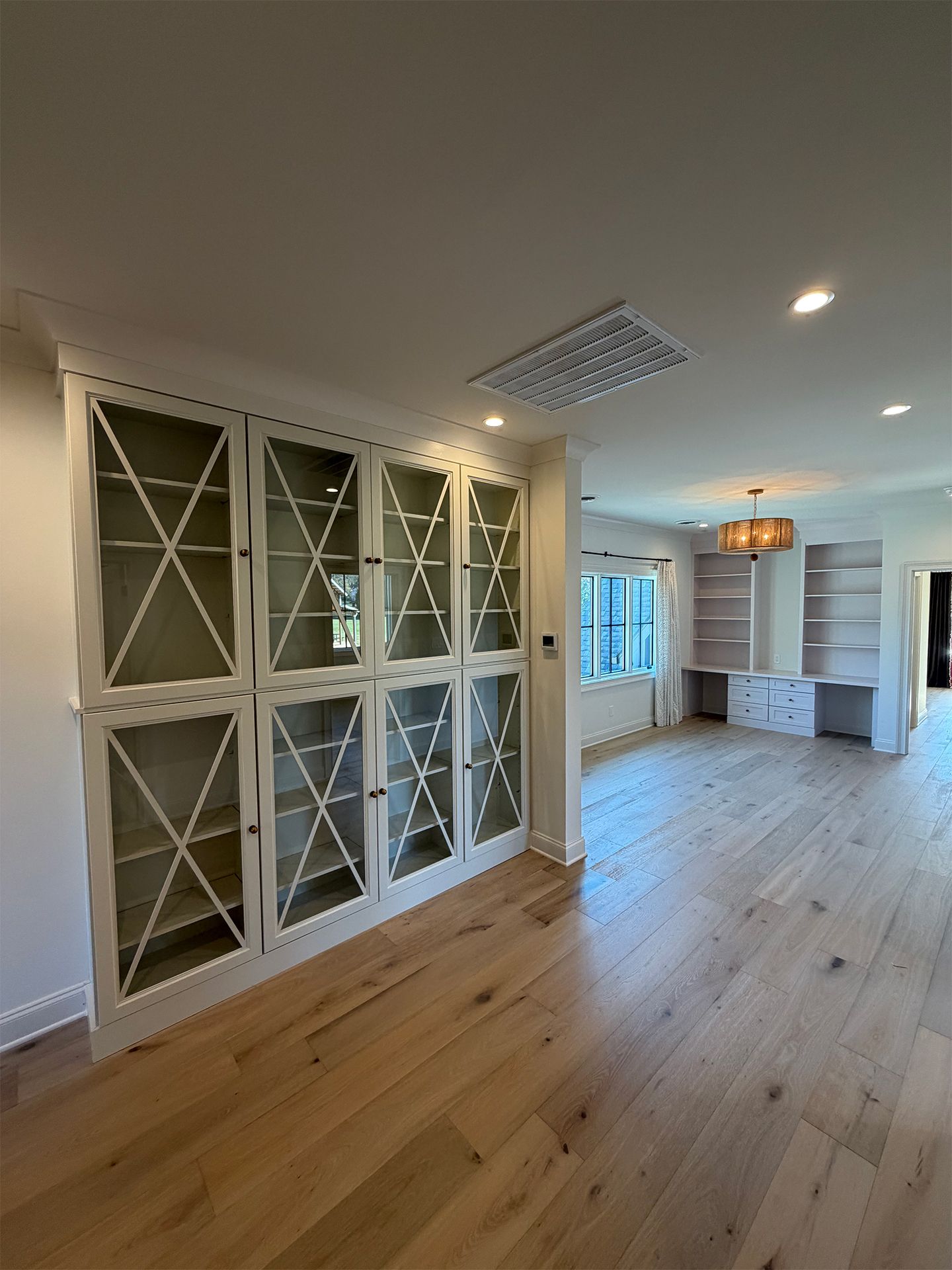 Empty modern room with light wood floors, white built-in cabinets, and a decorative glass-front partition