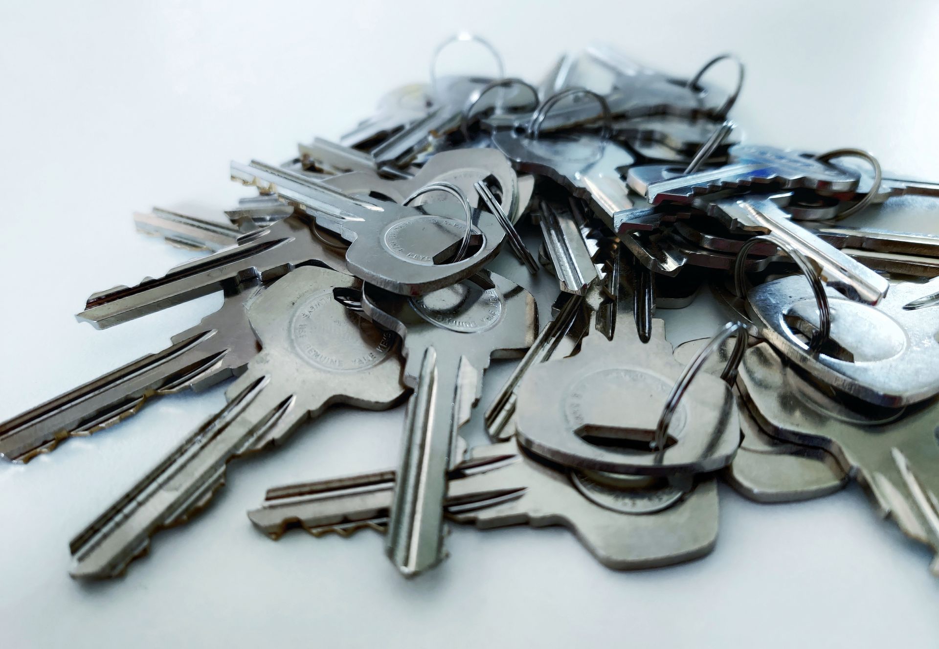 Pile of shiny metal keys on a white surface, various sizes and shapes.