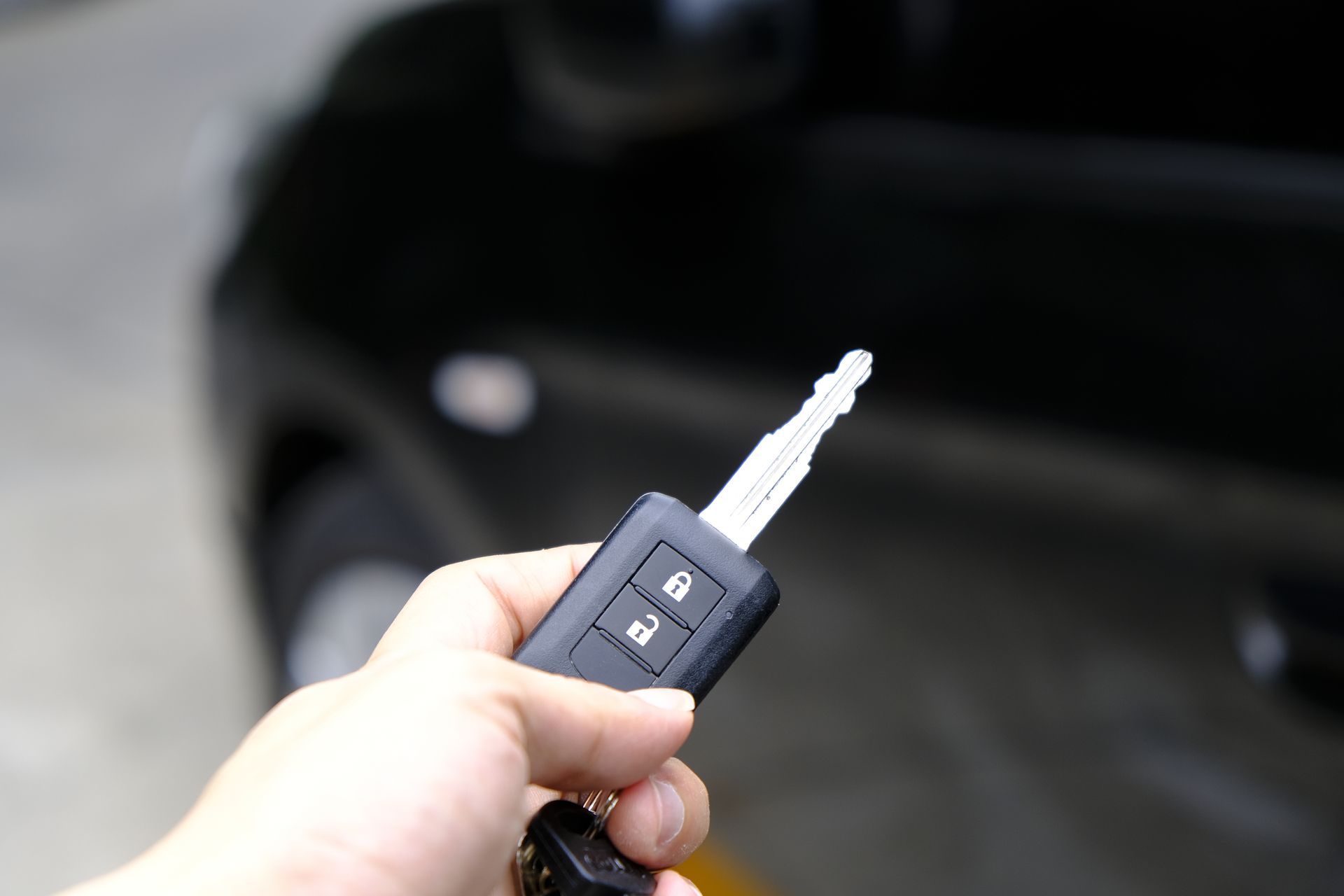 Hand holding a black car key with remote, near a black car door.