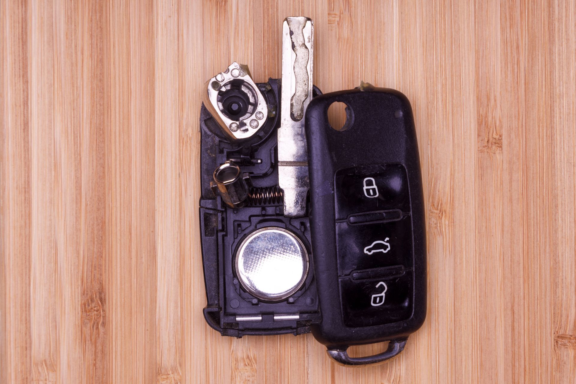 Broken car key on a wooden surface, showing internal components and key fob.