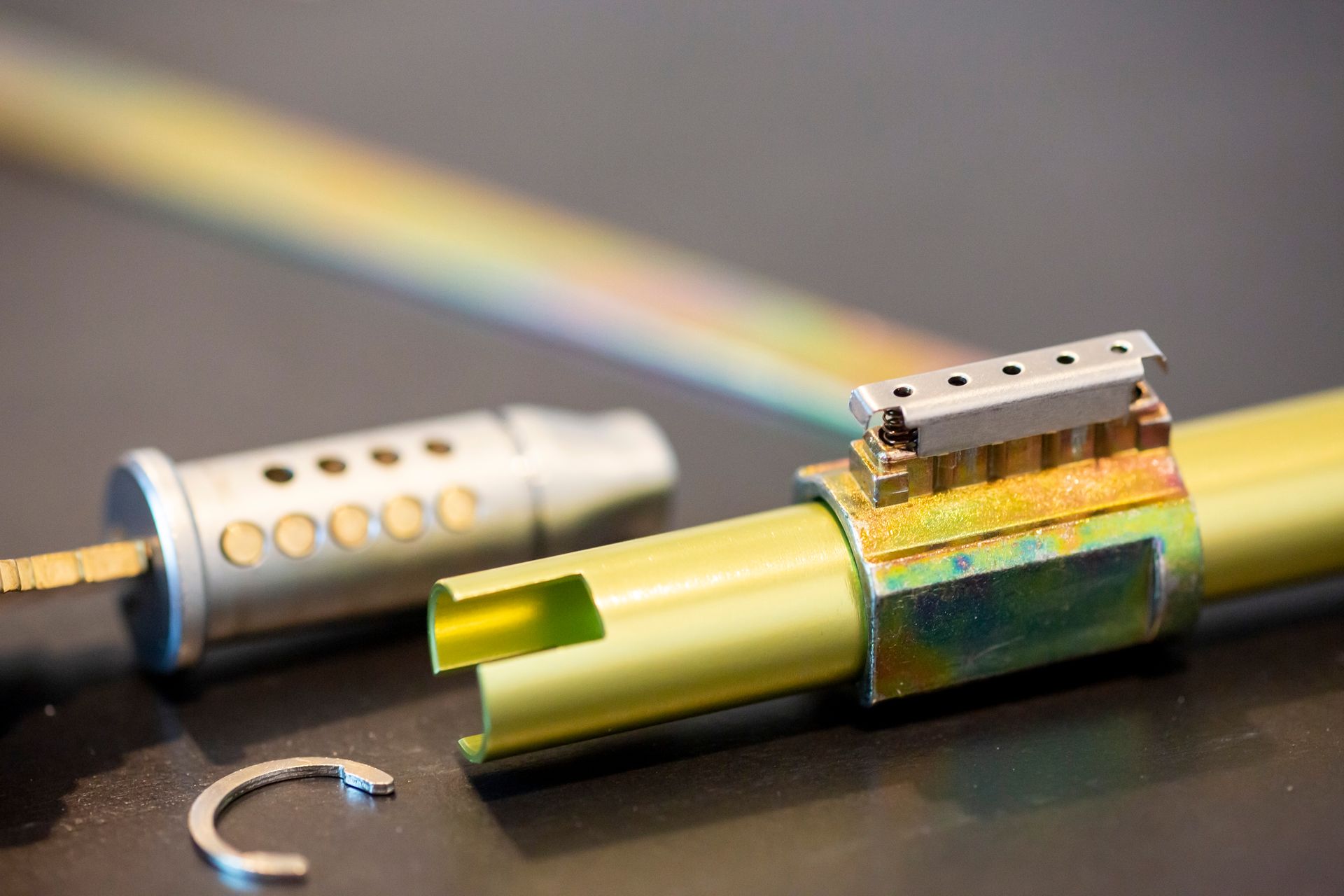 Disassembled lock components: tubular key, barrel, yellow metal tube, and retaining ring.