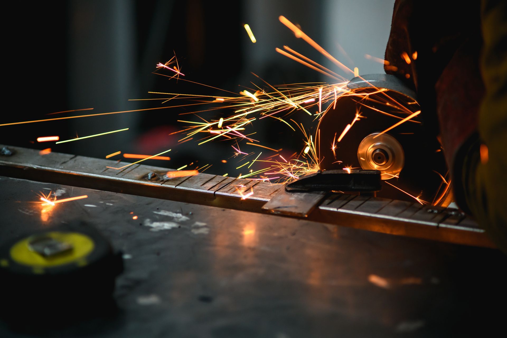 Sparks fly as a metal worker grinds a metal bar with a power tool, workbench, close-up.