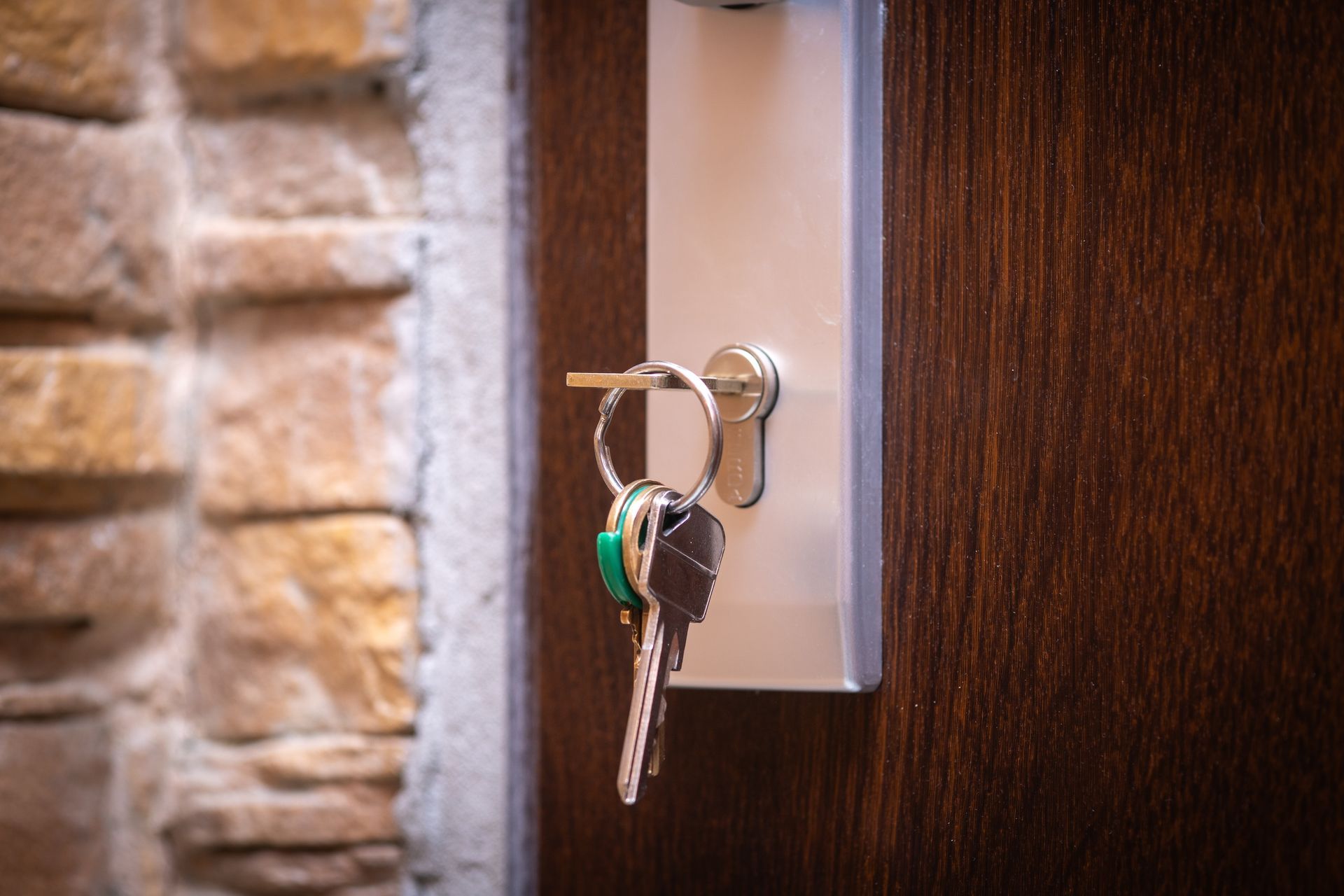 Keys in door lock, next to a stone wall and a dark wood door.