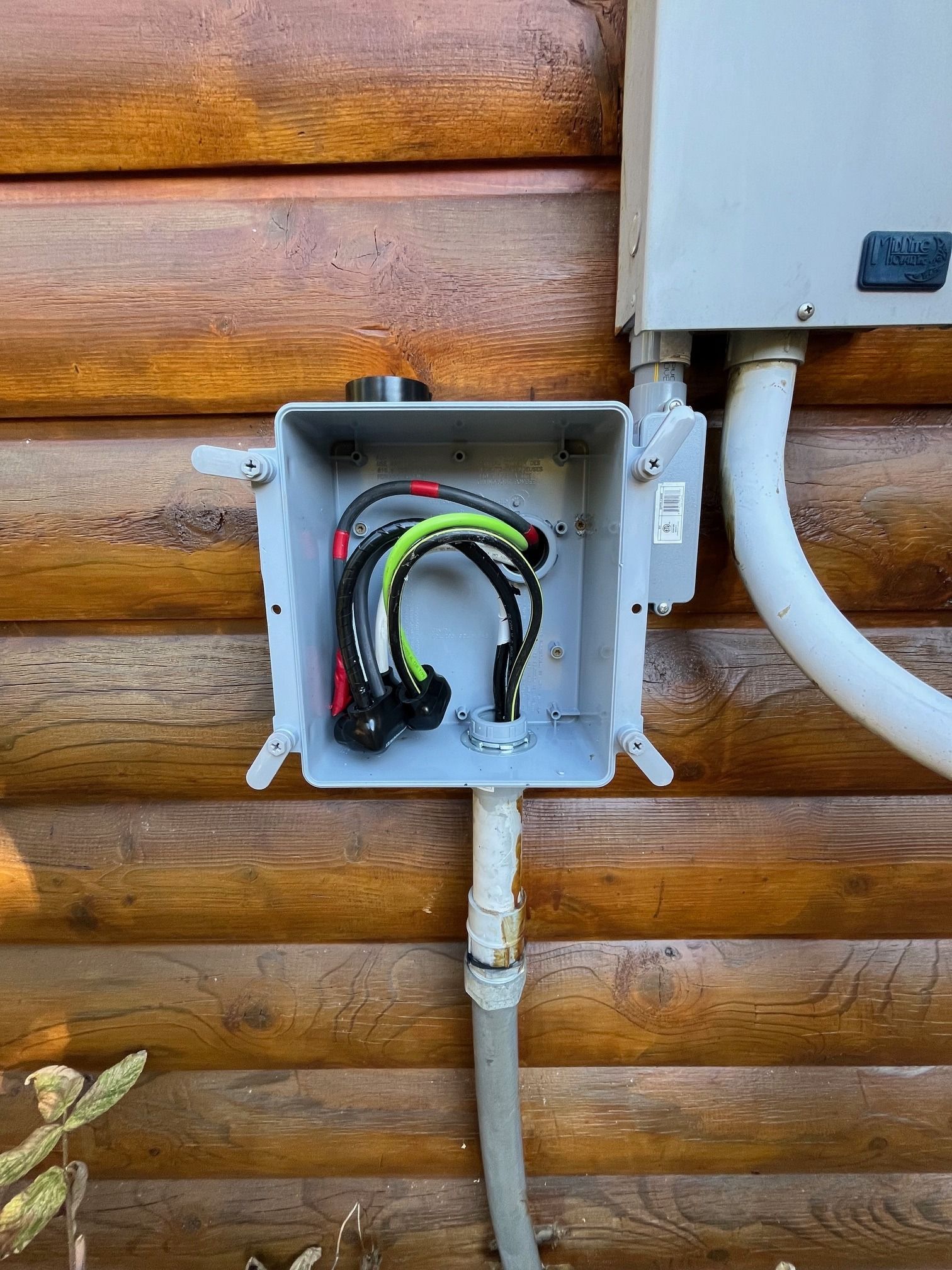 A box with wires coming out of it is attached to a wooden wall.