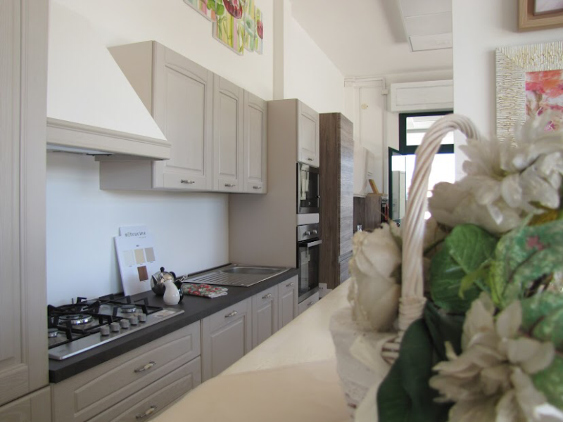 Cucina con mobili grigi, ripiani neri e cappa bianca. In primo piano un cesto di fiori.