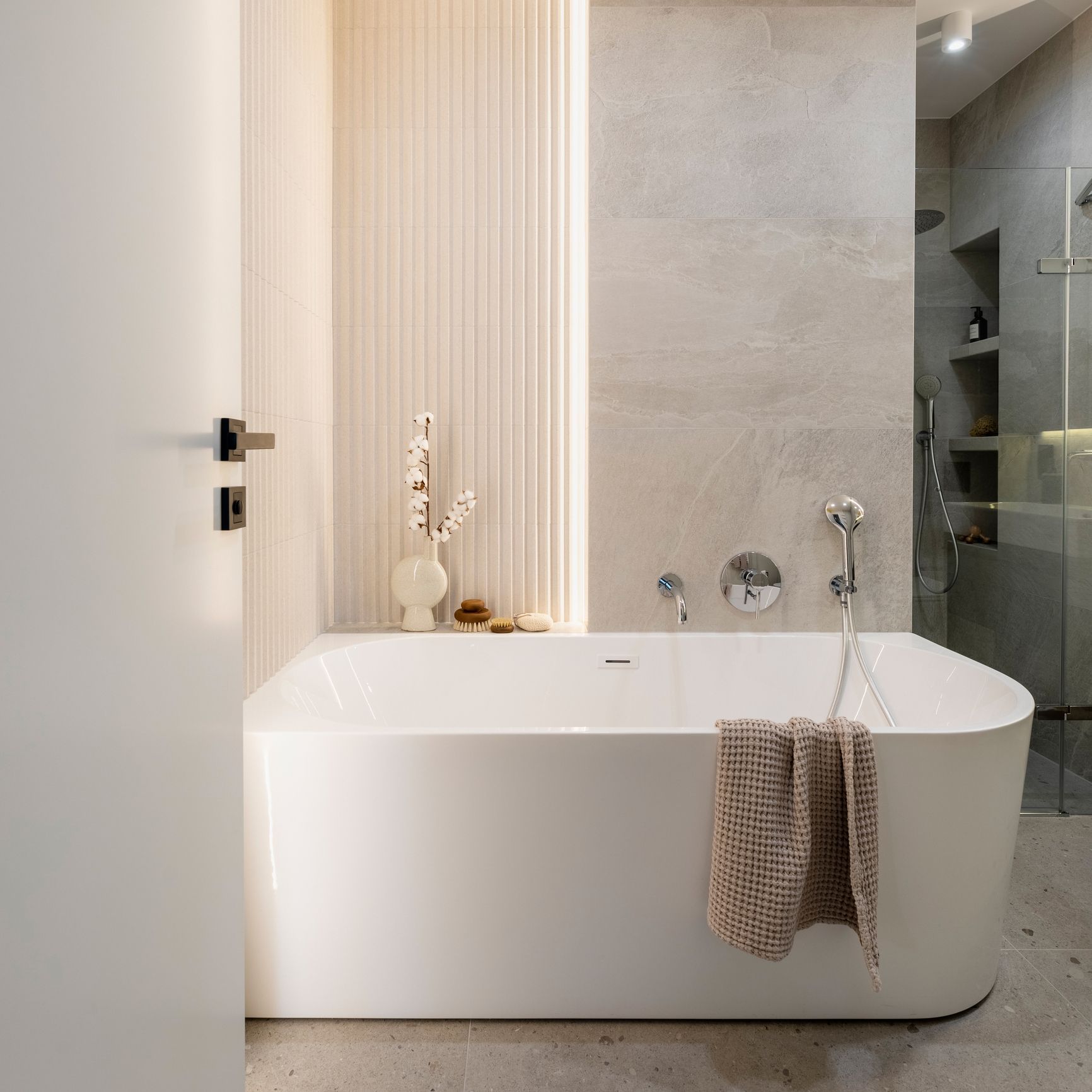 Bagno moderno con vasca bianca, pareti beige e doccia in vetro.