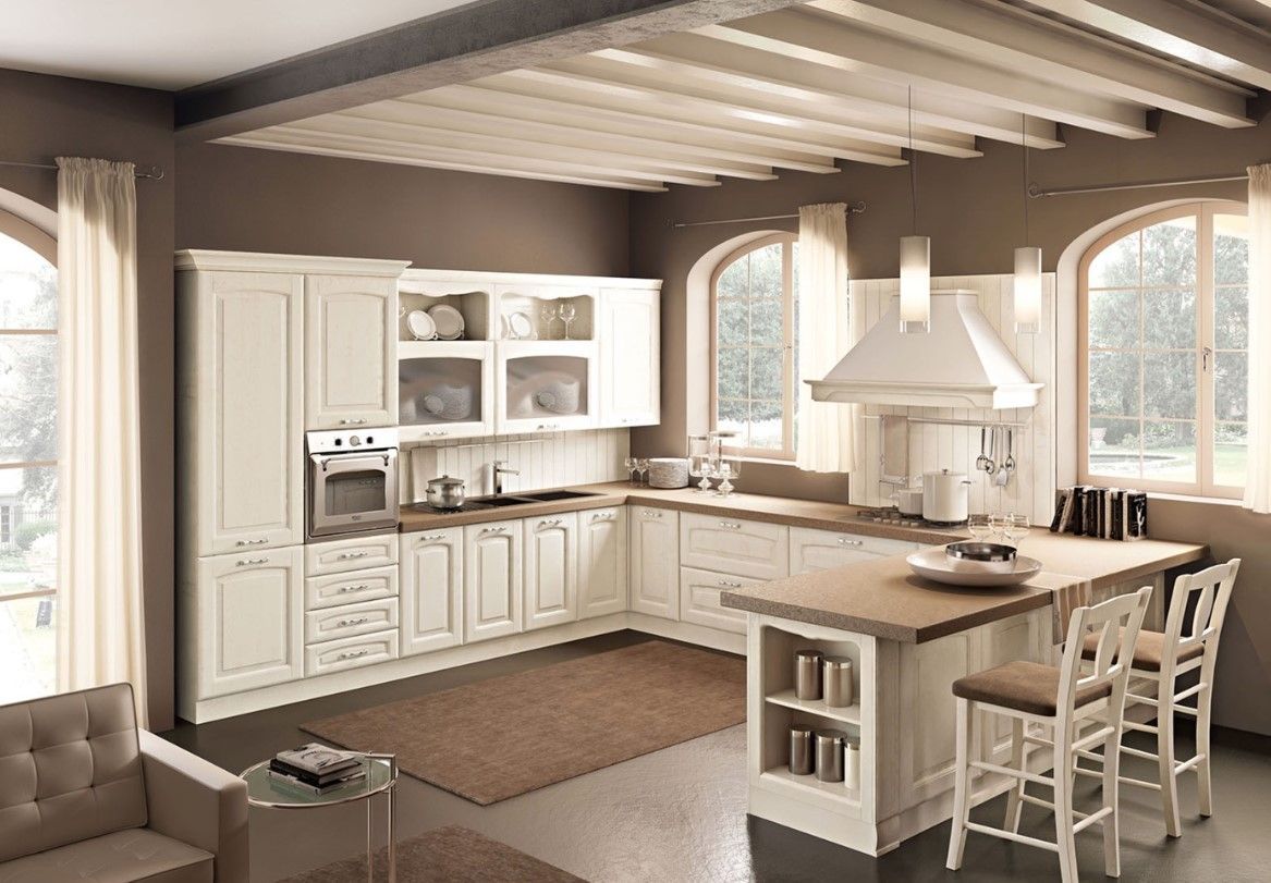 Cucina color crema con isola centrale e travi in legno. Due finestre ad arco forniscono luce naturale.