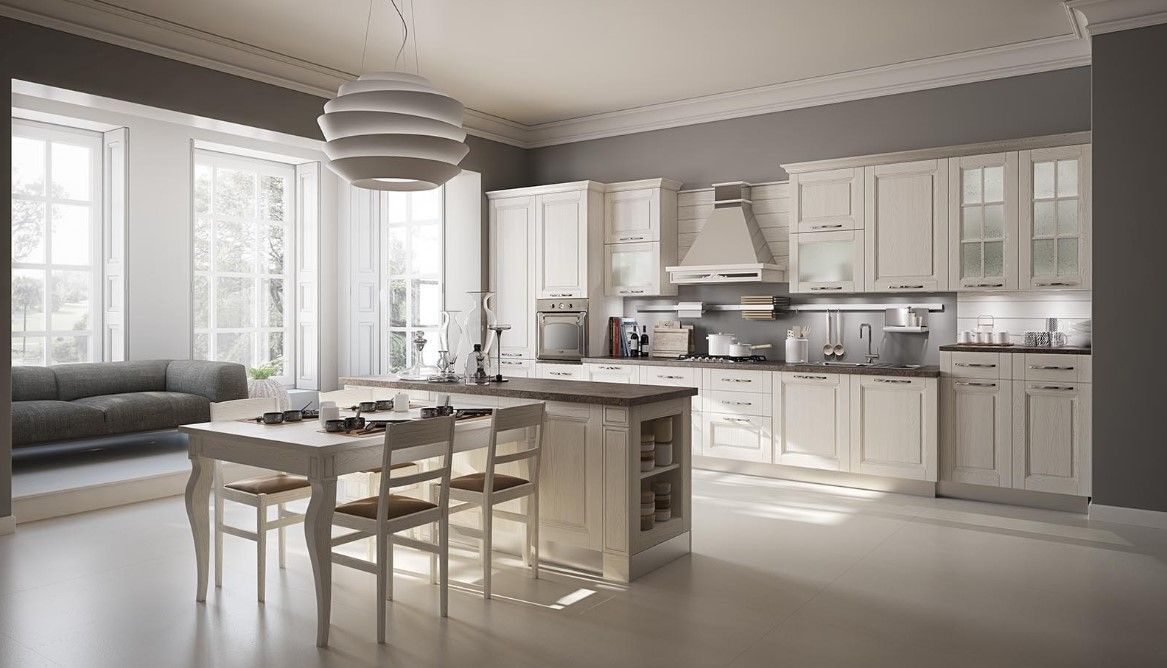 Elegante cucina bianca con isola, tavolo e divano; pareti grigio chiaro e ampie finestre.