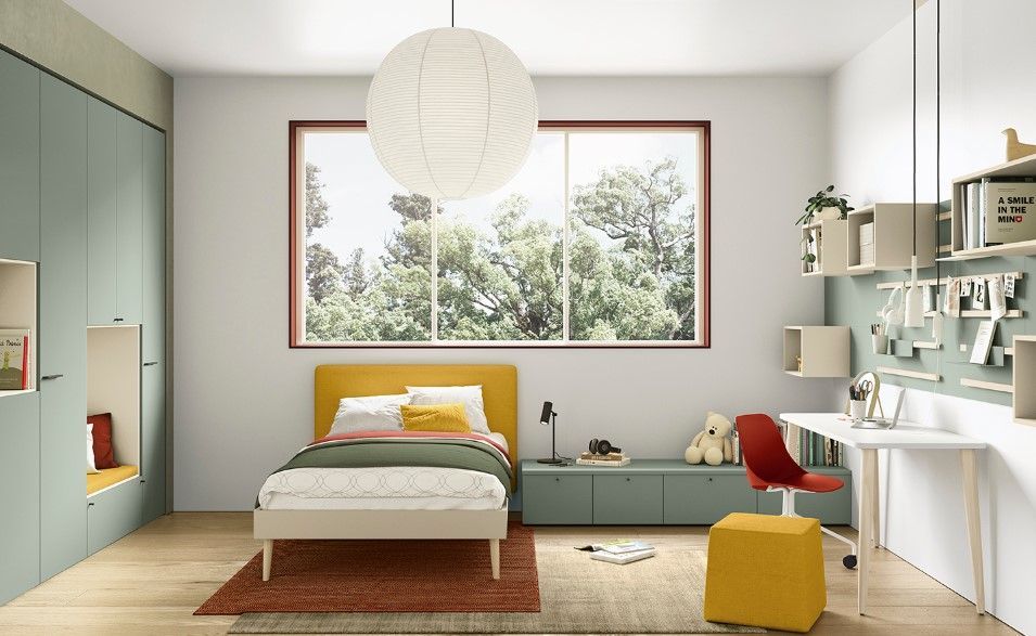 Comodino giallo con due cassetti e una piccola lampada, accanto a un letto con testiera verde acqua e decorazione murale raffigurante una bicicletta.