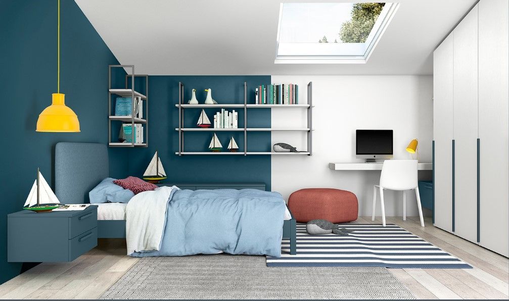 Camera da letto con pareti blu e bianche, letto, scrivania, scaffali e lucernario.