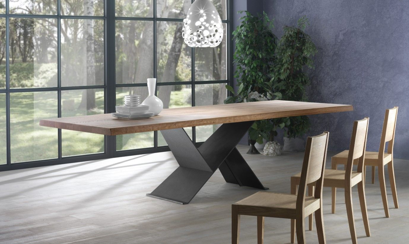 Tavolo da pranzo in legno con base in metallo a forma di X, quattro sedie e grande finestra con vista sugli alberi.