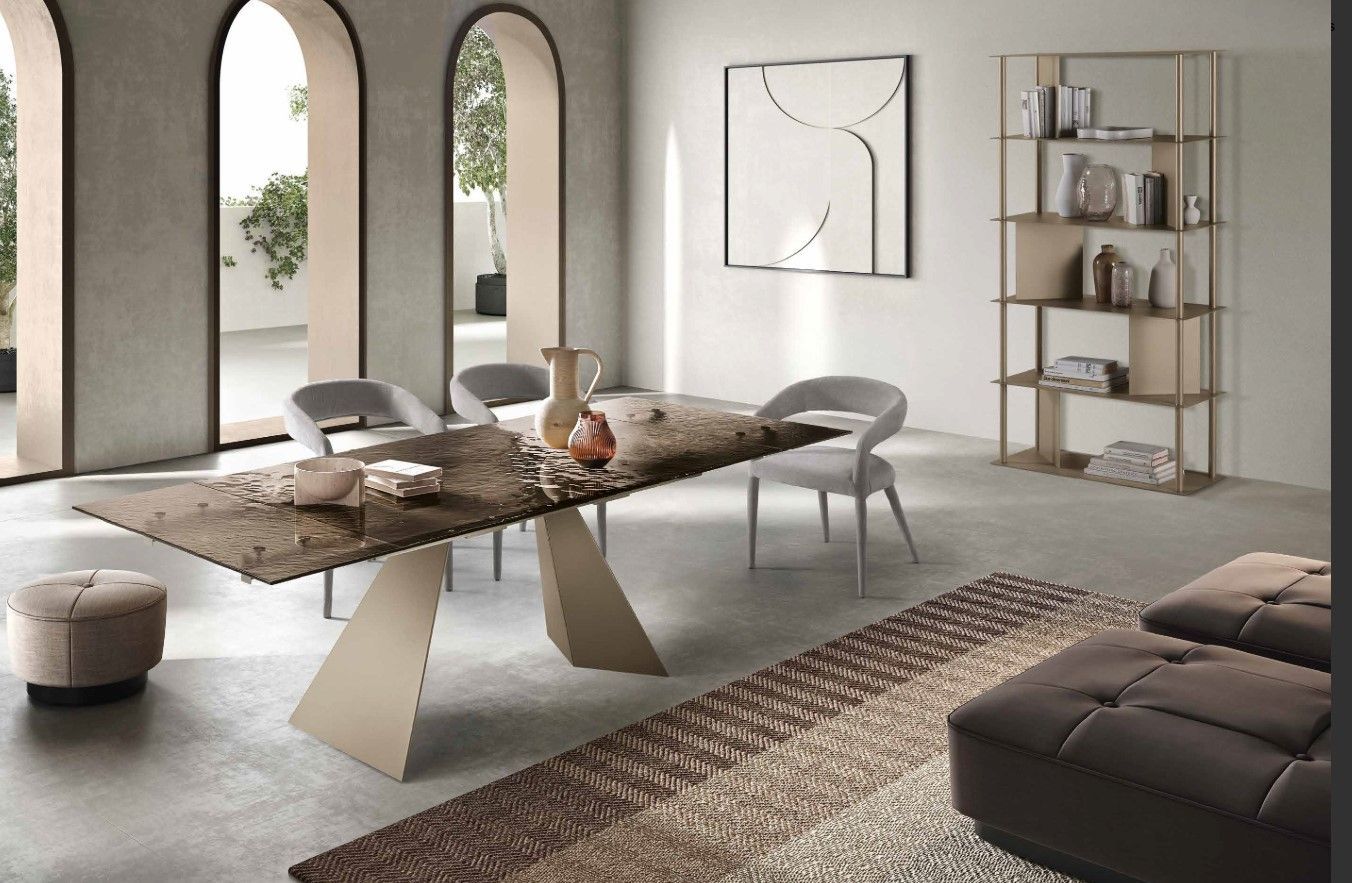 Sala da pranzo con un lungo tavolo, sedie, tappeto e una libreria. Colori neutri.