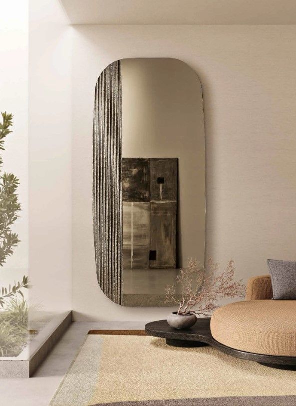 Specchio ovale a figura intera con pannello laterale metallico testurizzato in un moderno spazio abitativo.