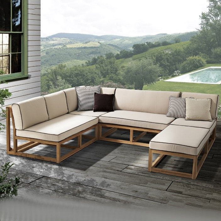 Divano componibile da esterno con cuscini beige, struttura in legno e vista sulla campagna.