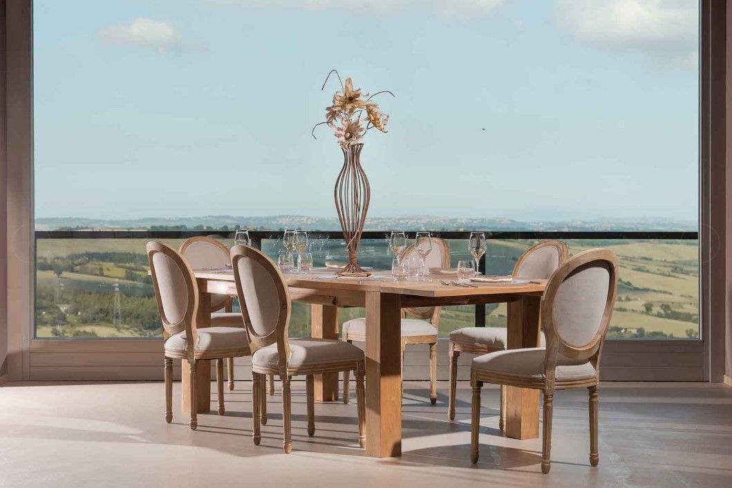 Tavolo da pranzo apparecchiato per sei persone con centrotavola floreale, sullo sfondo di una vista panoramica all'aperto.