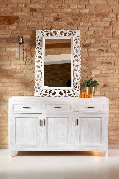 Credenza in legno bianco con specchio contro una parete di mattoni, arance e una pianta sopra.