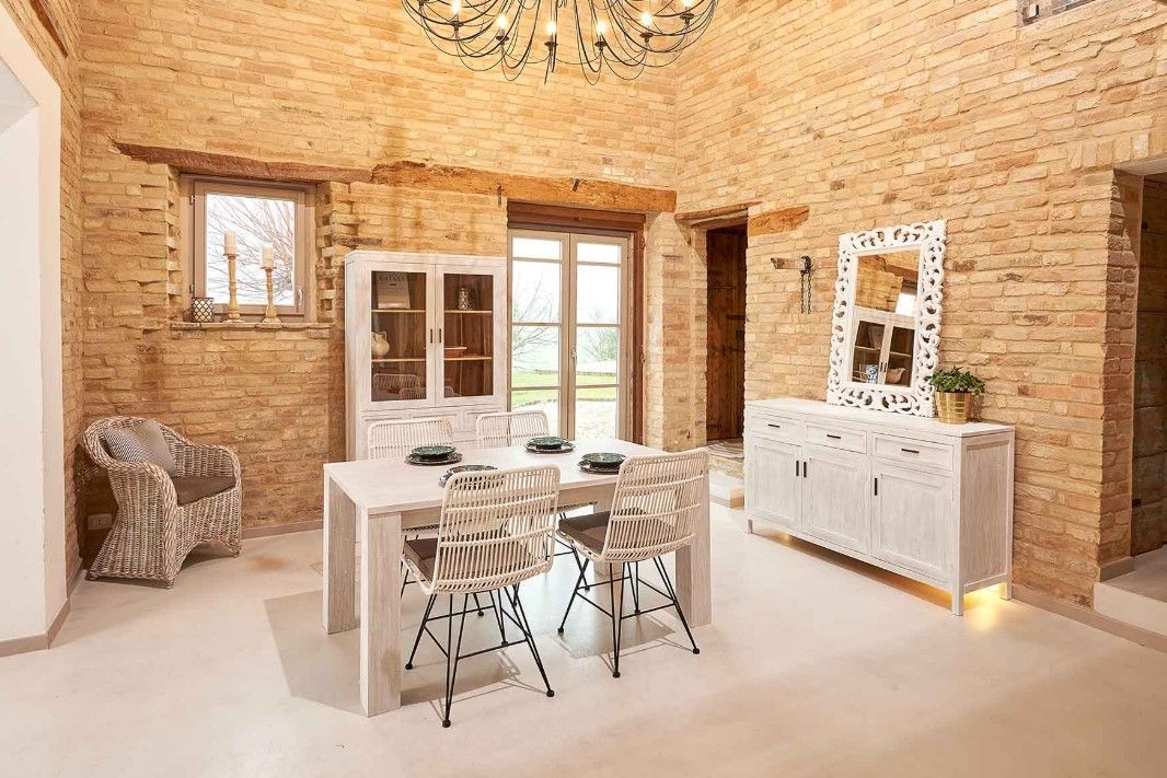 Sala da pranzo con pareti in mattoni a vista, mobili bianchi e un lampadario.