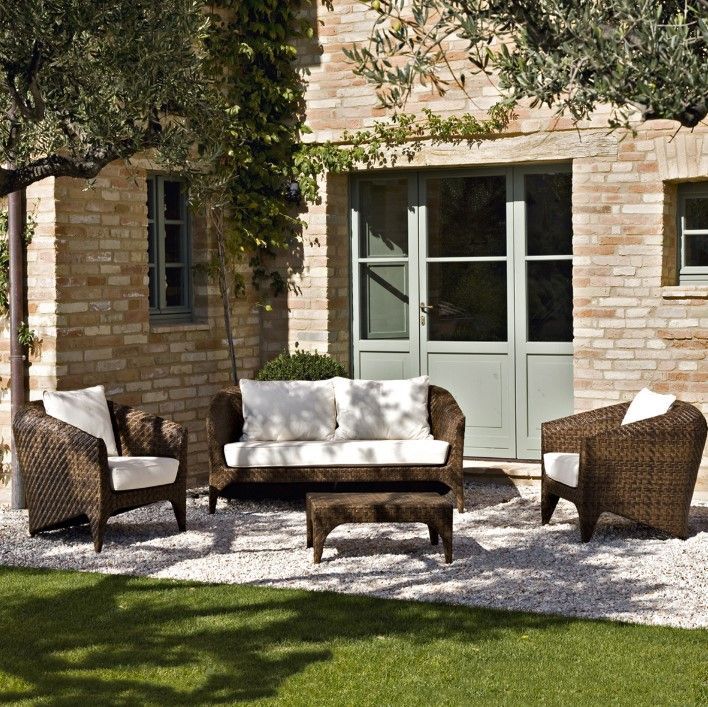 Arredi da esterno in vimini su patio in ghiaia, sfondo di un edificio in mattoni, prato verde, soleggiato.