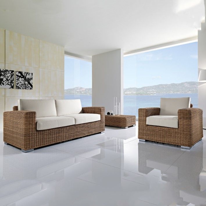 Soggiorno con divano in rattan, poltrona e tavolino da caffè; cuscini bianchi, pavimento bianco lucido, ampie finestre con vista sull'oceano.