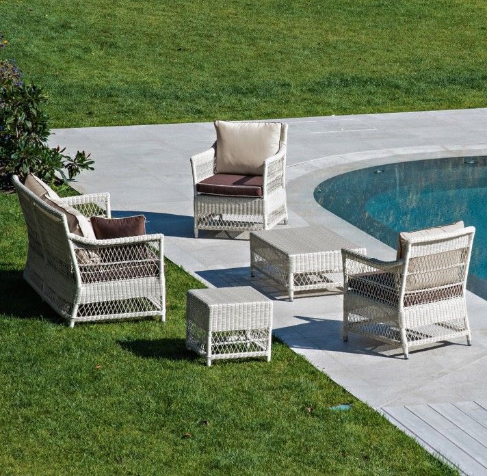 Set di mobili da giardino in vimini vicino a una piscina. Include un divano, due sedie e due tavolini su erba e cemento.