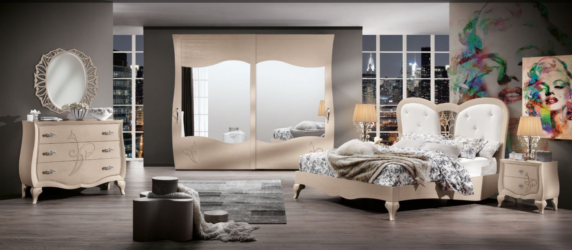 Camera da letto con mobili decorati color crema: letto, cassettiera, comodino e armadio. Quadri astratti appesi alla parete.