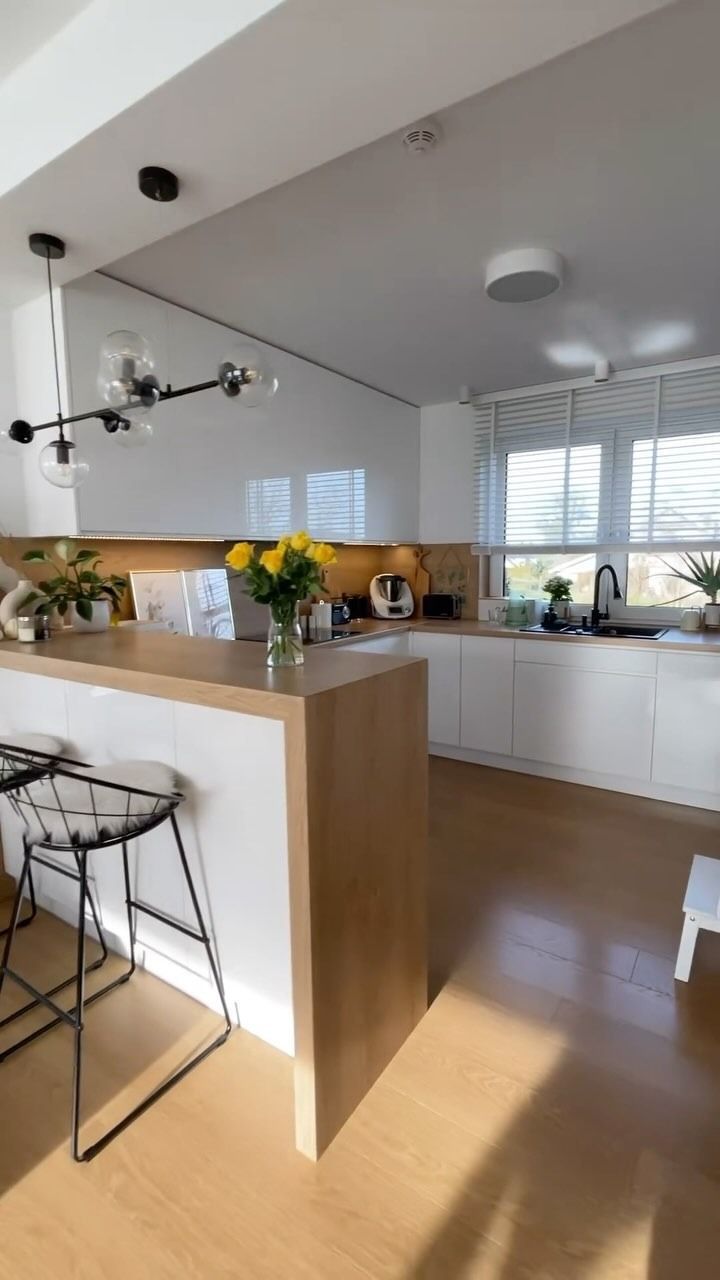Cucina luminosa e moderna con mobili bianchi, isola in legno e fiori gialli sul bancone.