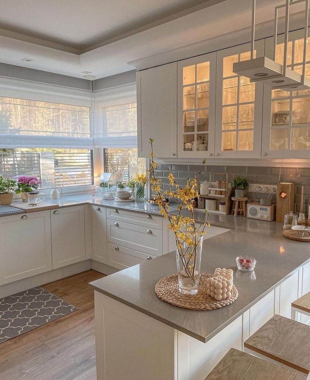 Cucina bianca con ripiani in granito, mobili con ante in vetro e fiori gialli sull'isola.