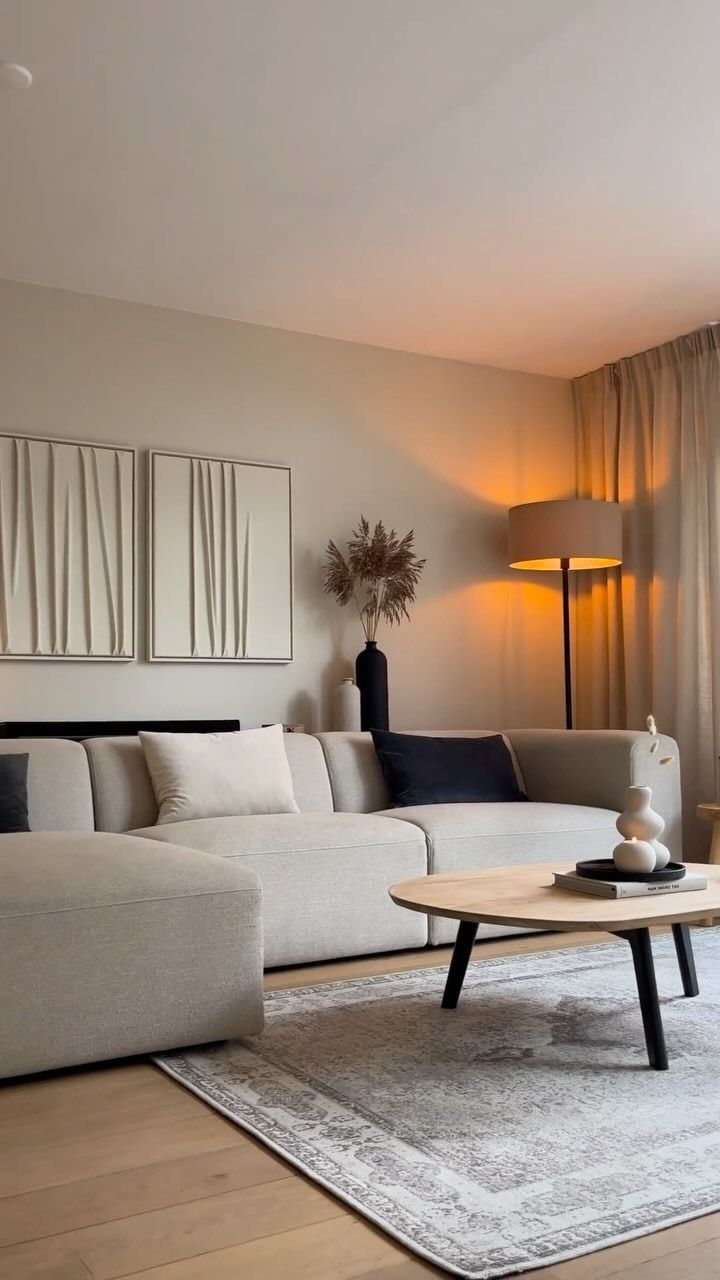 Soggiorno con divano chiaro, tavolino, tappeto e opere d'arte. Luci calde e toni neutri.