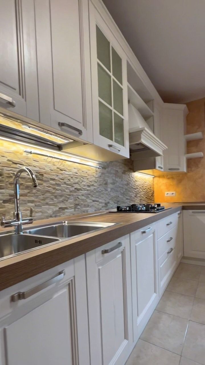 Mobili da cucina bianchi con ripiani in legno, paraschizzi in pietra e lavello in acciaio inossidabile.