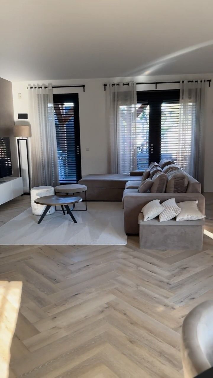 Soggiorno con divano componibile beige, tavolino da caffè e pavimento in legno a spina di pesce.