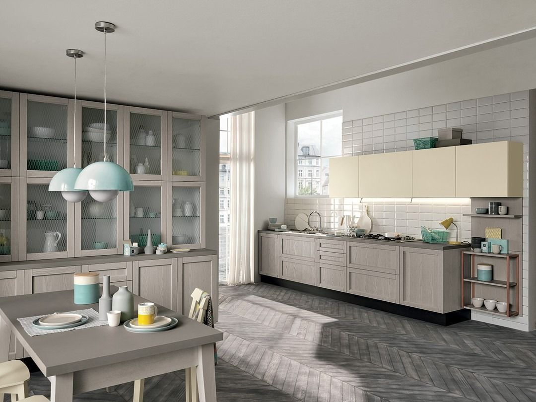 Interno della cucina con mobili, tavolo e isola in tonalità neutre, pavimento in legno decorato e finestra.