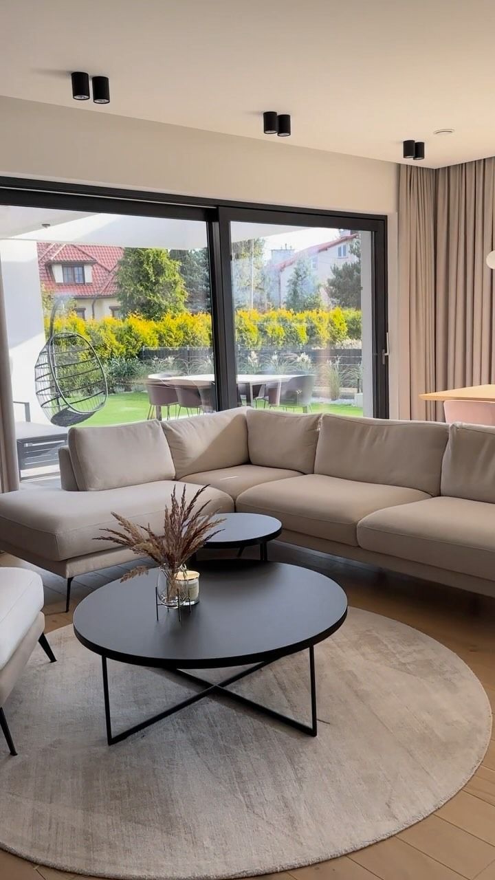 Soggiorno con divano componibile beige, tavolini neri e ampia finestra con vista sul cortile.