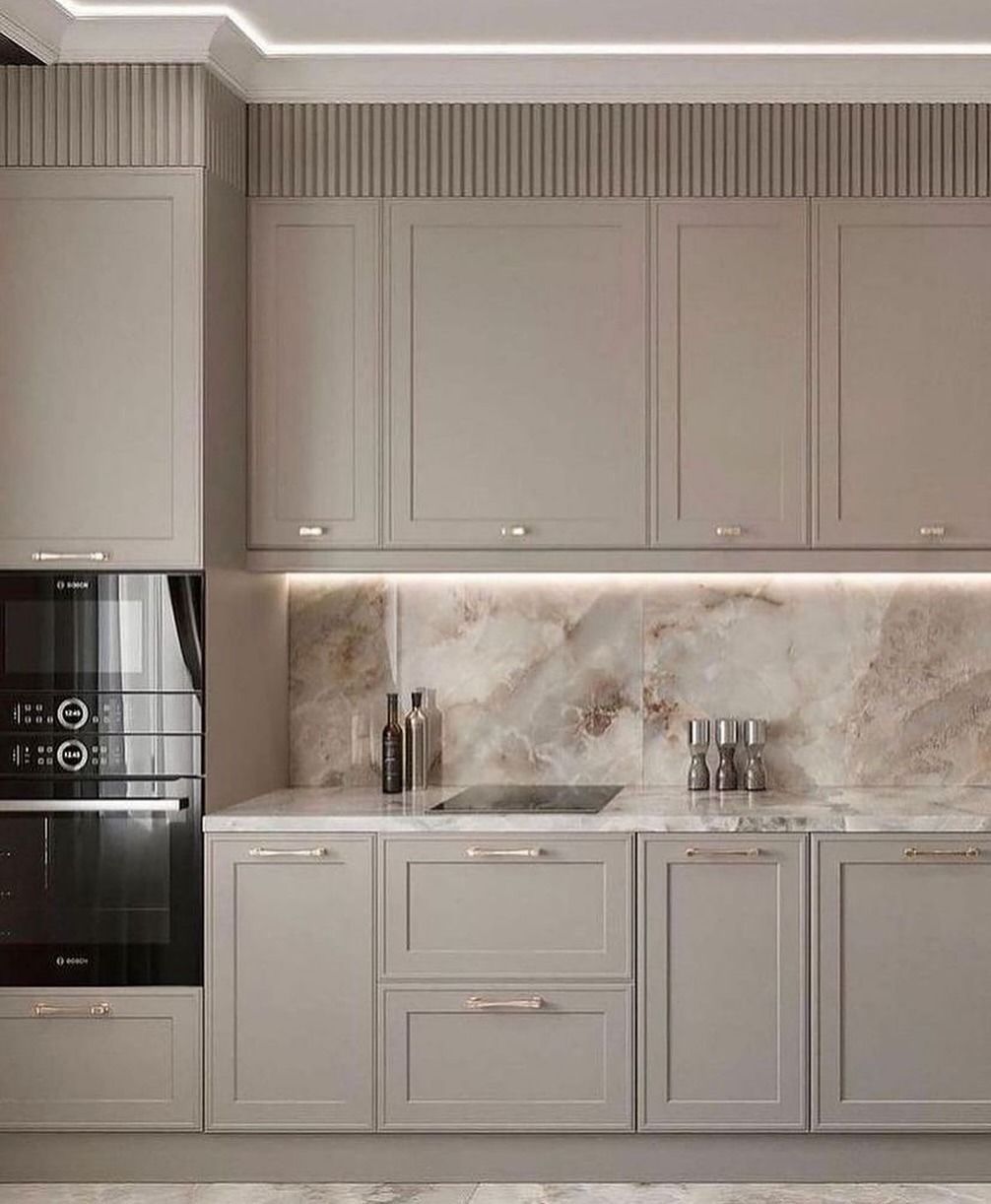 Cucina moderna con mobili grigio chiaro, paraschizzi in marmo e forno incorporato.