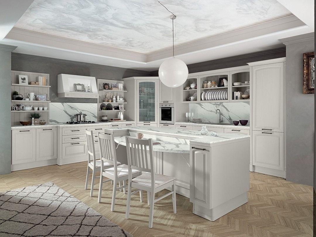 Cucina bianca con isola, ripiani in marmo, mobili bianchi e sedie.