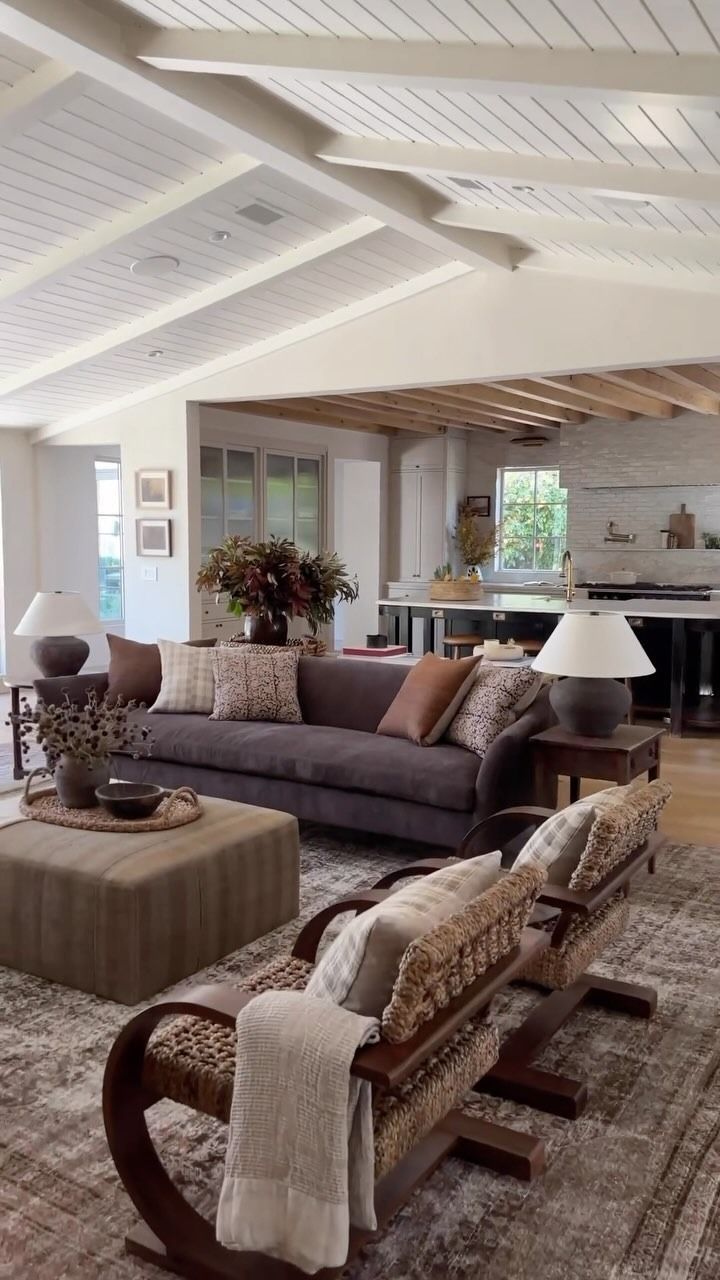 Soggiorno con divano grigio, sedie a fantasia e un tappeto neutro sotto un soffitto con travi bianche.