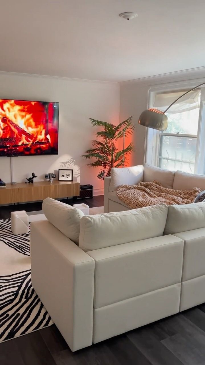 Accogliente soggiorno con divano componibile bianco, scena del camino in TV e tappeto con stampa zebrata.