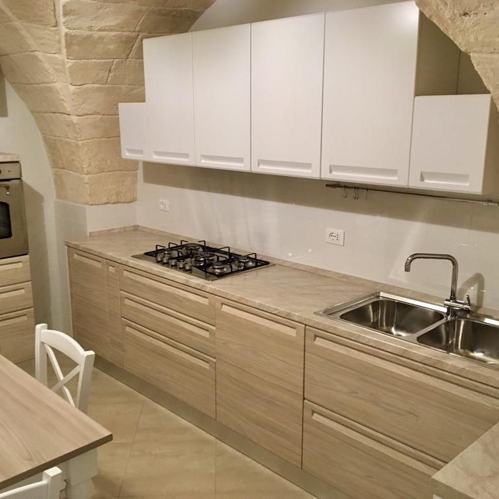 Cucina moderna con mobili in legno chiaro, pensili bianchi, arco in pietra e lavello in acciaio inossidabile.
