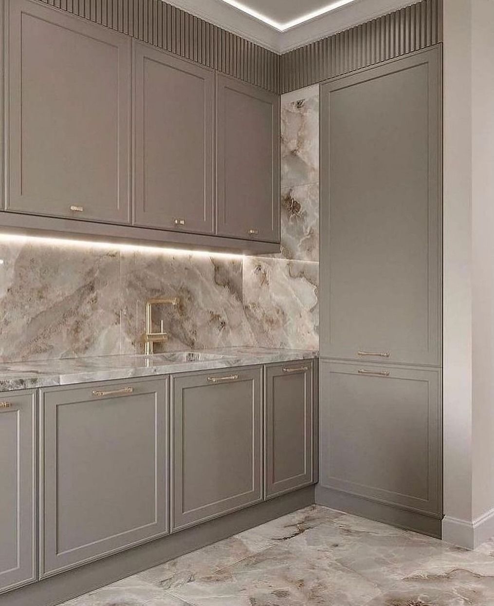 Una cucina moderna con mobili grigi, paraschizzi in marmo e ferramenta dorata.