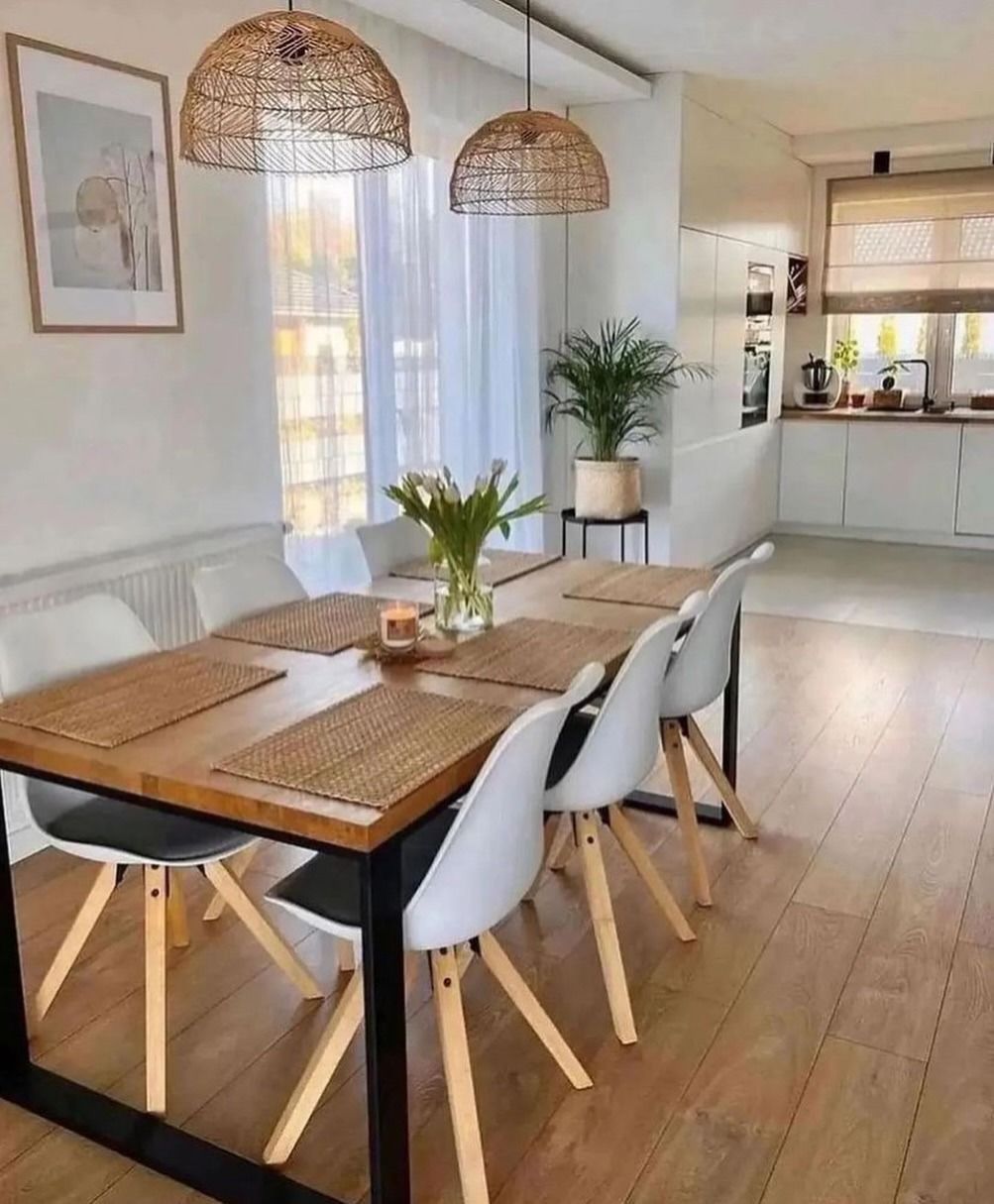 Sala da pranzo con tavolo in legno, sedie bianche, lampade a sospensione intrecciate e cucina sullo sfondo.