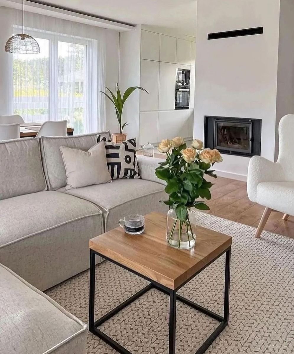 Soggiorno dai toni neutri. Divano beige, tavolino in legno, camino e poltrona bianca.