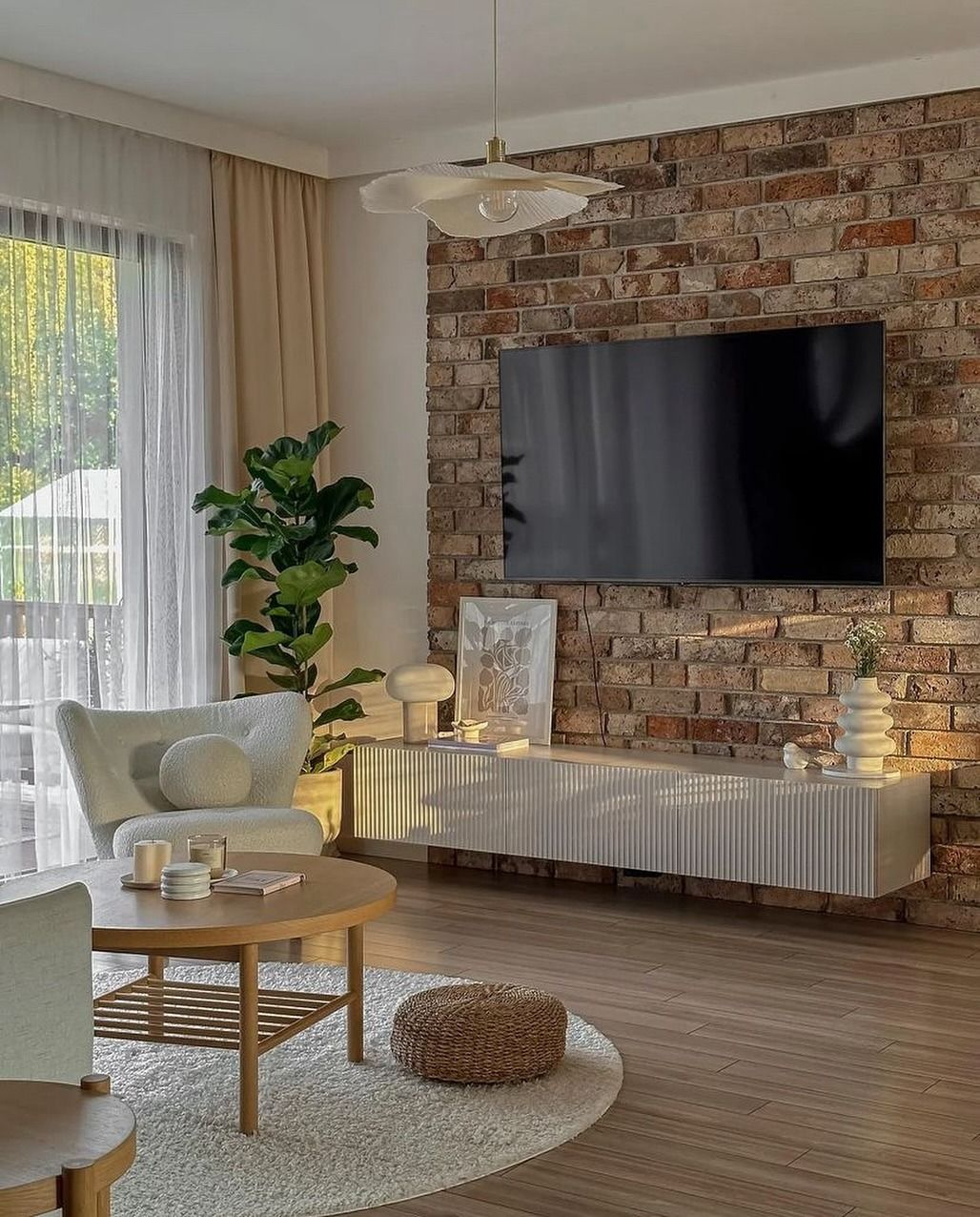 Soggiorno con parete in mattoni a vista e TV montata sopra un mobile bianco.
