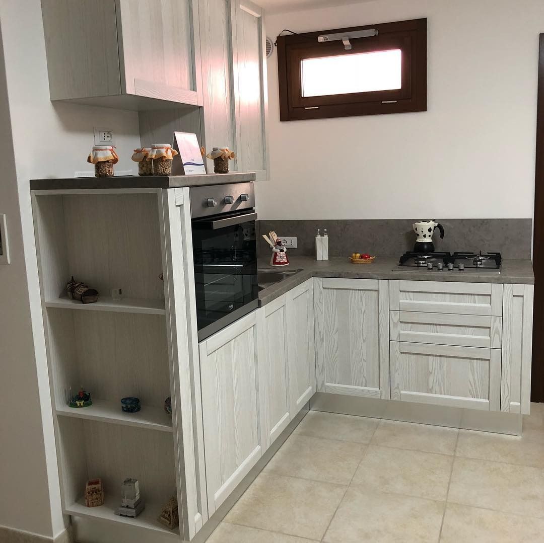 Mobili da cucina bianchi con forno incorporato, piano di lavoro, ripiani aperti e piccola finestra.